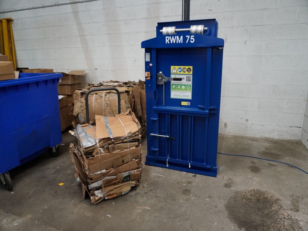 a blue waste baler next to a bale of cardboard. 