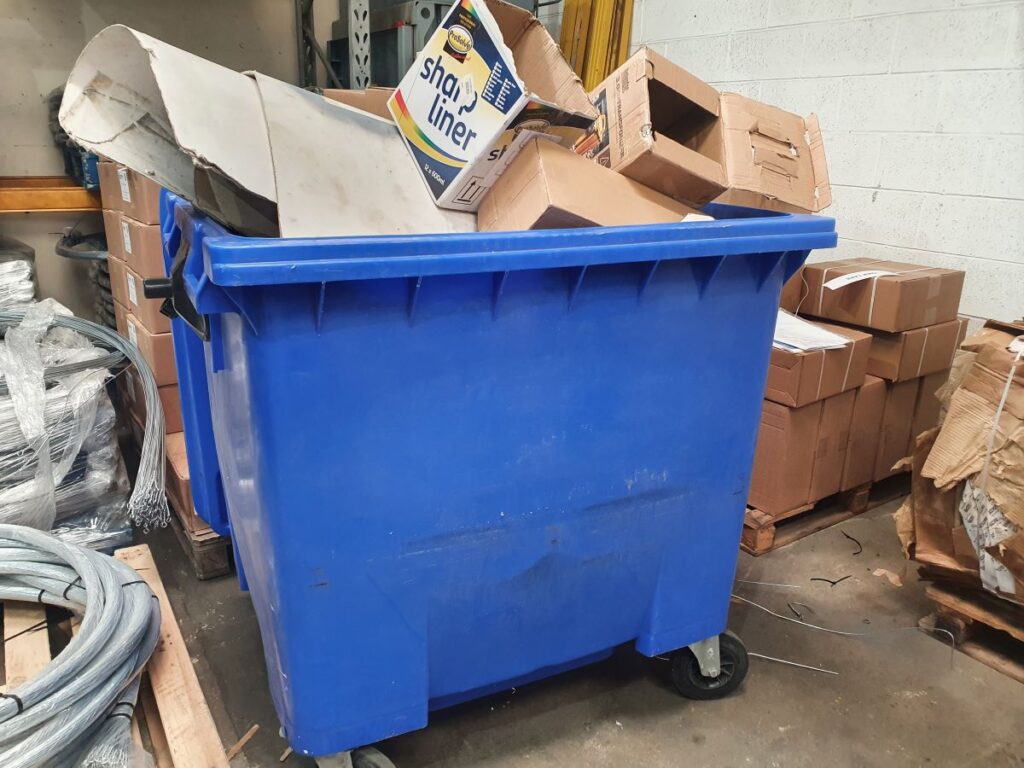 a blue waste bin filled overflowing with cardboard boxes