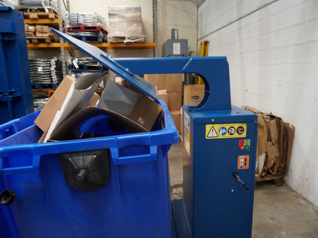 a waste management equipment, called a bin press, with a cardboard waste bin next to it