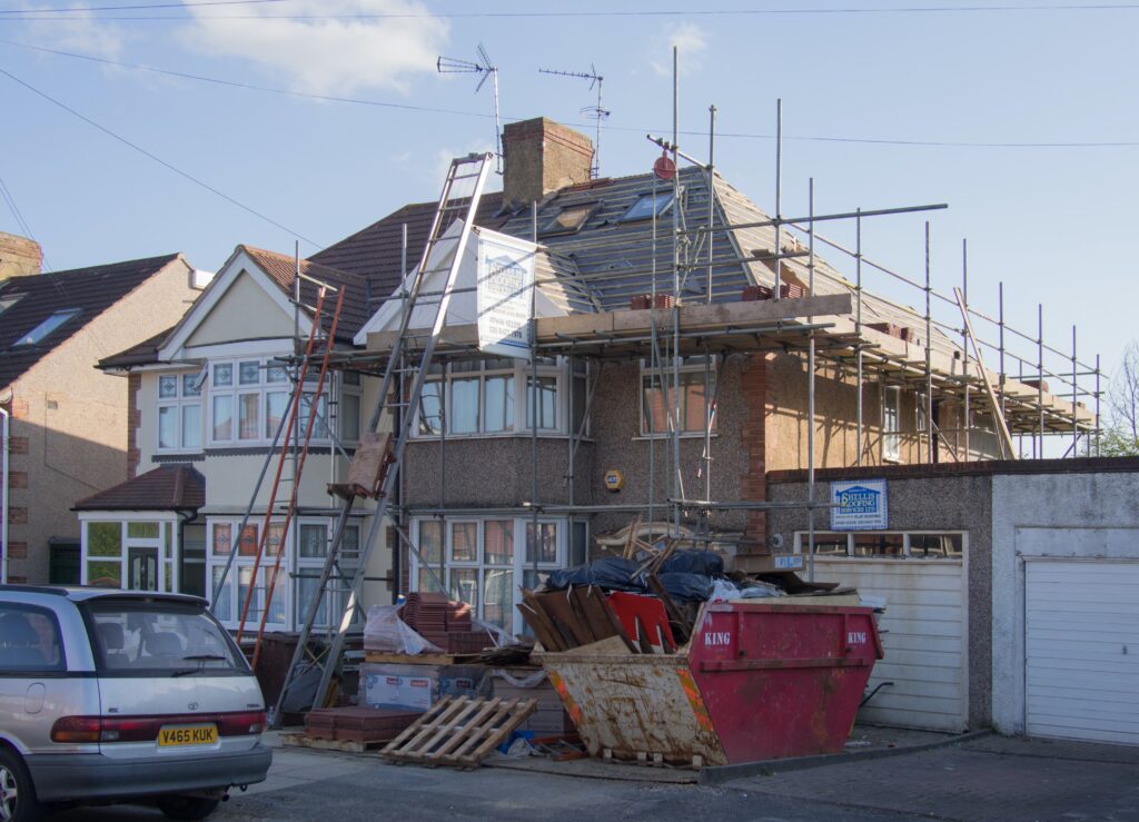 A house with scaffolding on it. There is also a full skip in front of the house.