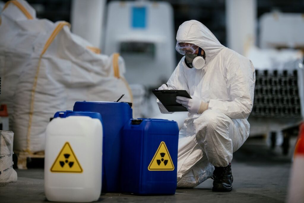 A man crouched down wearing the PPE needed to dispose of asbestos correctly. In front of him are containers labelled as hazardous