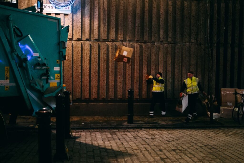 Two men throwing a box into the back of a bin lorry used by a licenced waste carrier.