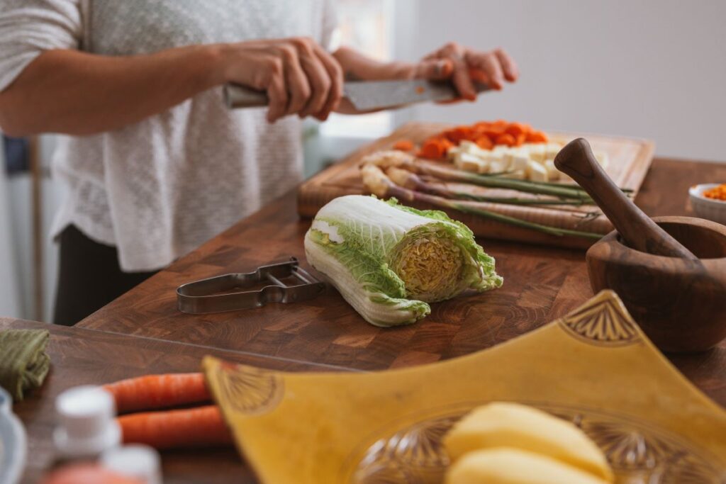 A woman cutting vegetables on a chopping board next to food waste