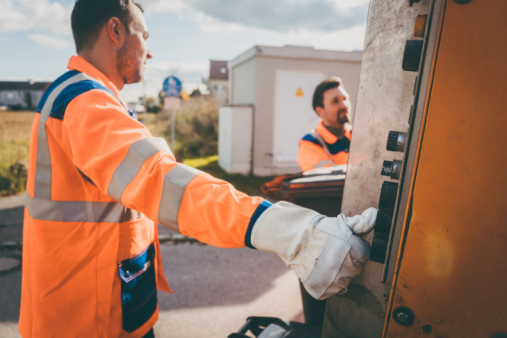 A man in hi-vis pressing a button on the back of a waste collection truck