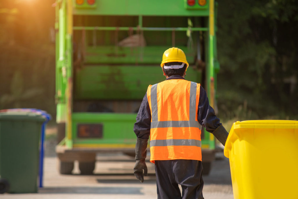 A man in hi-vis jacket carrying a bin towards a waste collection lorry