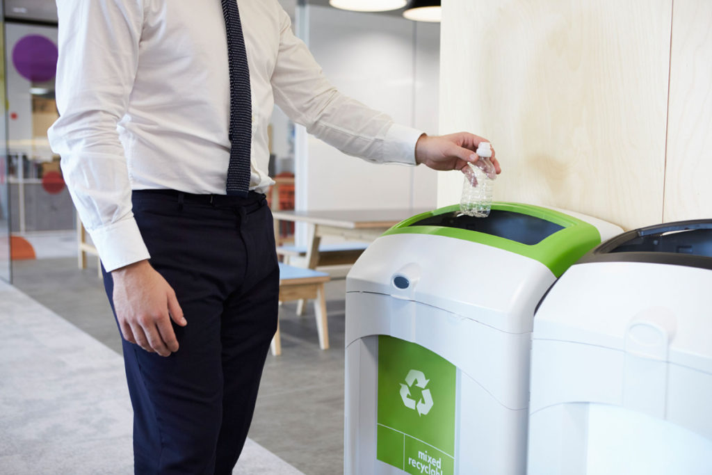 A man in a suit putting a plastic bottle in a recycling bin