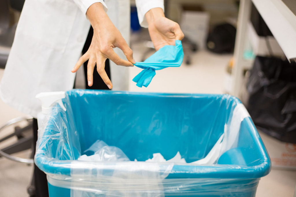 A woman taking off a glove and putting it in a clinical waste bin