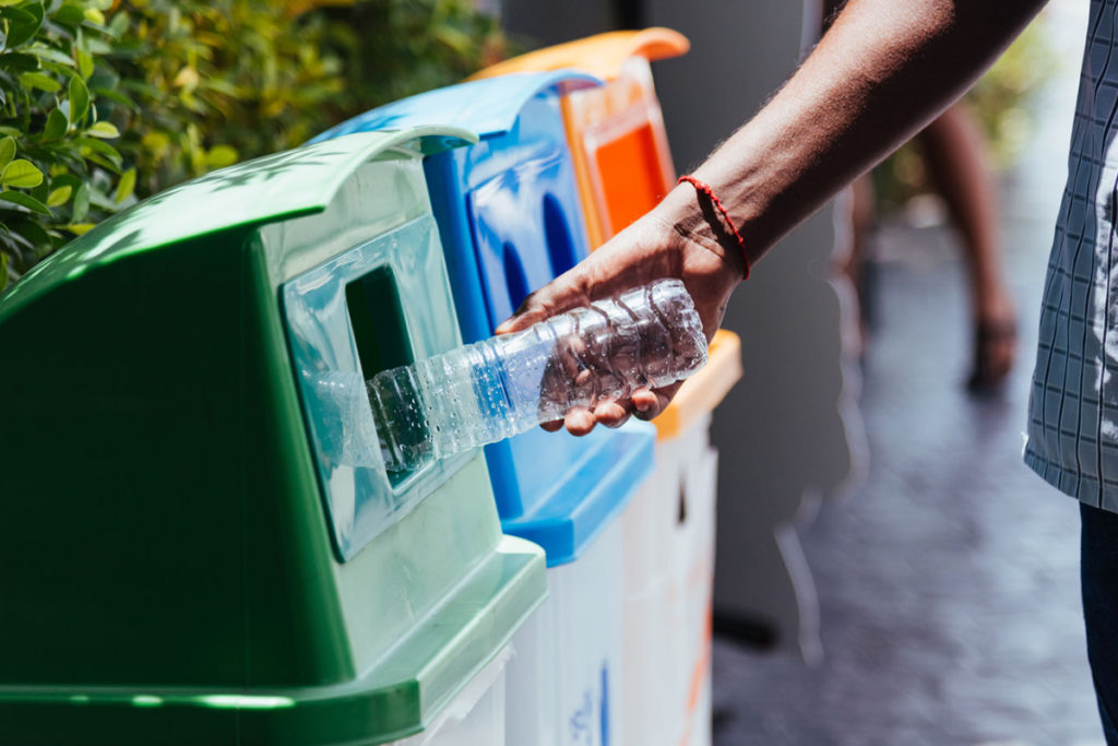 A hand putting a plastic bottle in the recycling bin