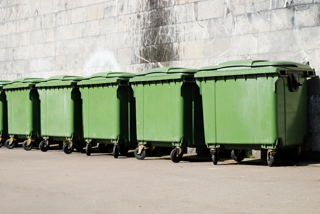 Green 1100L bins in a row outside next to a wall