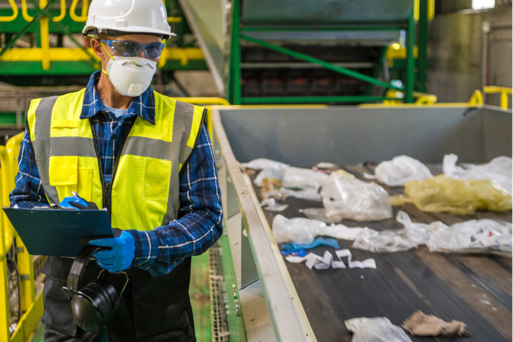 A man in a hardhat looking at waste on a conveyor belt